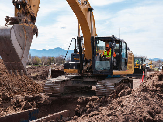 Cat excavator with steel track undercarriage digging on a construction site — aftermarket track chains, shoes, rollers, idlers, and sprockets for heavy equipment undercarriages