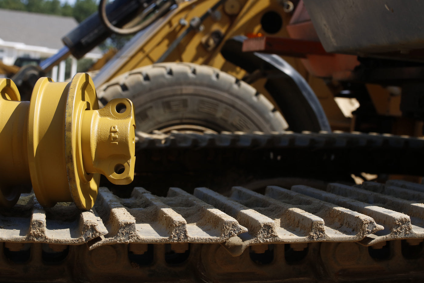 "Close-up of a yellow undercarriage track roller on a rubber track machine, with hydraulic boom and tire visible in the background